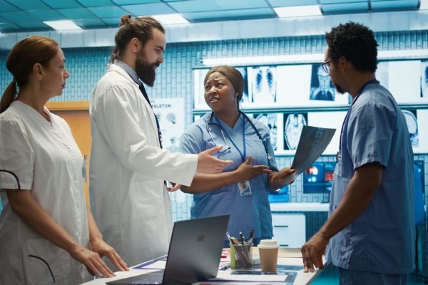 Hospital team examine x rays and discusses treatment strategy in a medical cabinet. Physicians with expertise in radiology and disease prevention doing collective work for health service. Camera B.